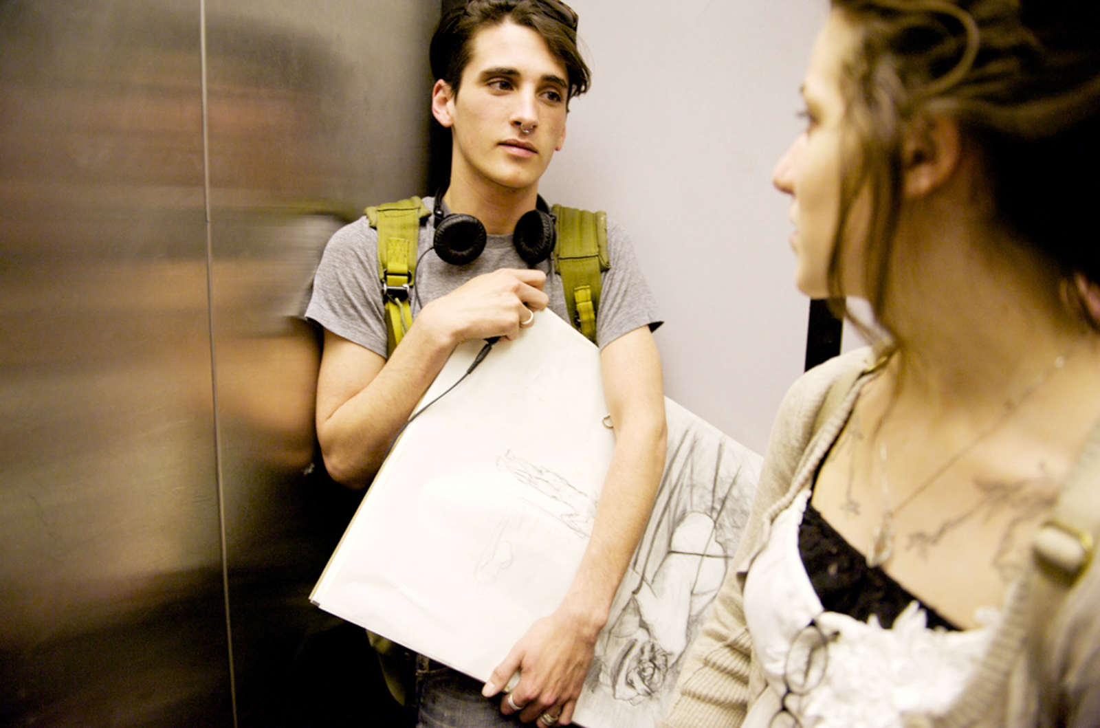 Male student in an elevator wearing headphones with female student looking back