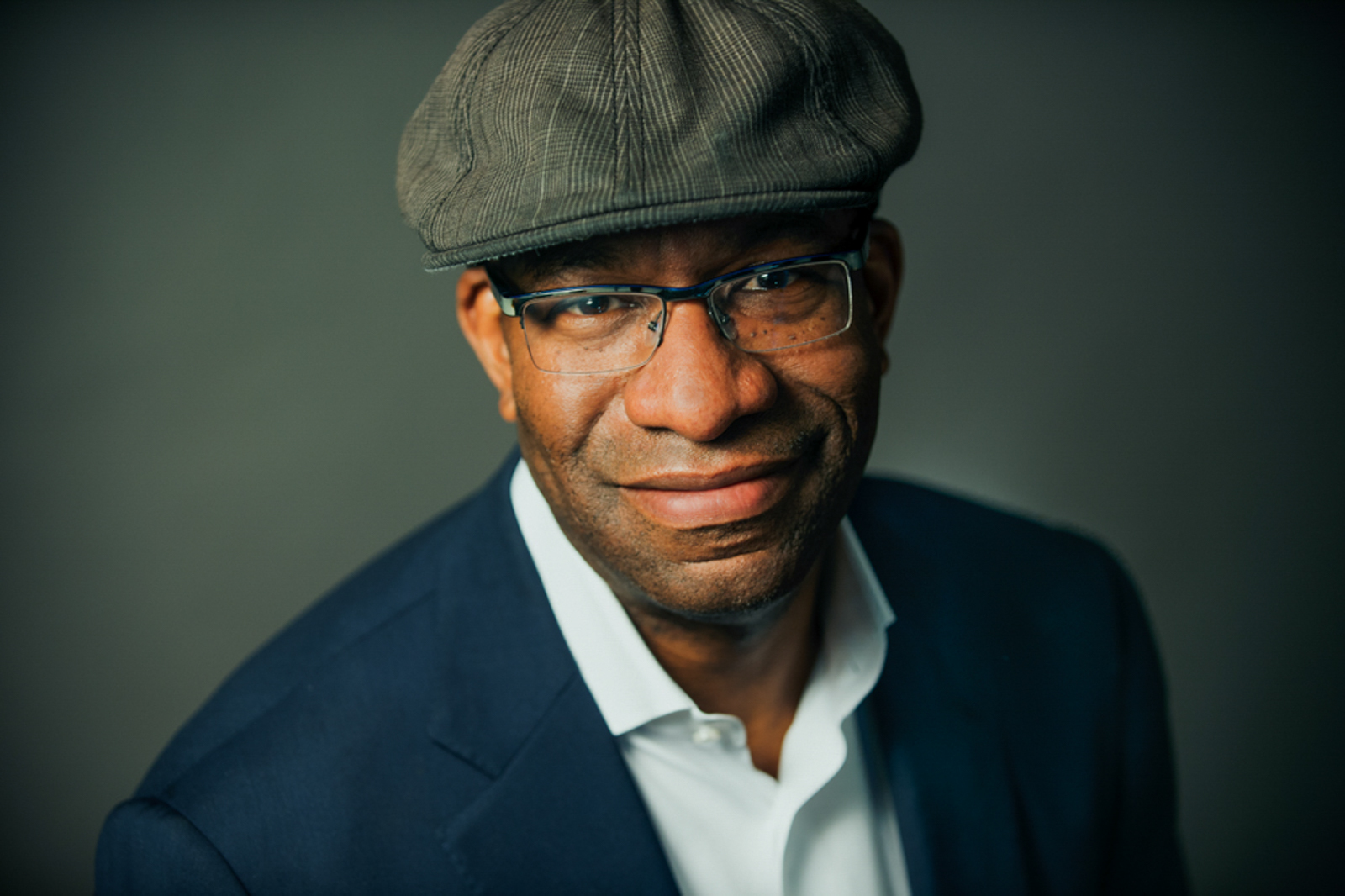 Portrait of a man wearing a hat and glasses with a soft smile