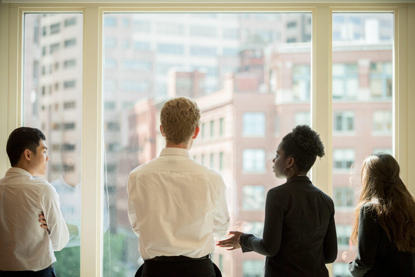 Image of four young people in a business setting looking outside a window