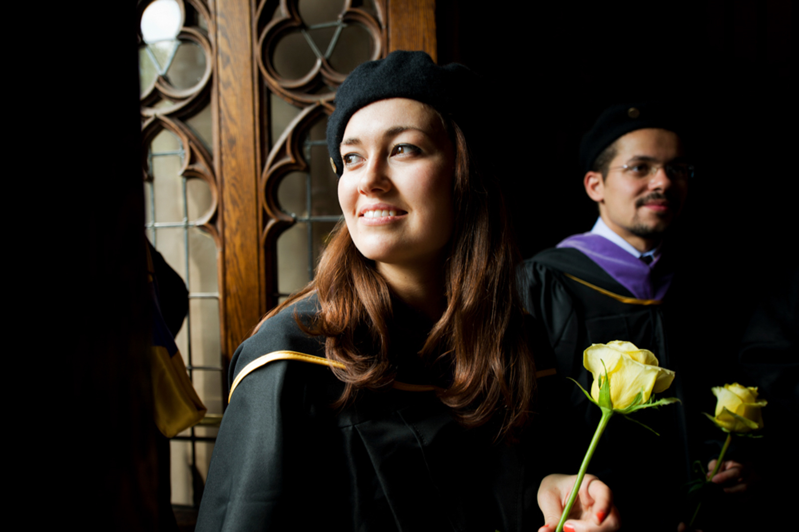 Graduating students in dim lit room female student in foreground holding flower smiling